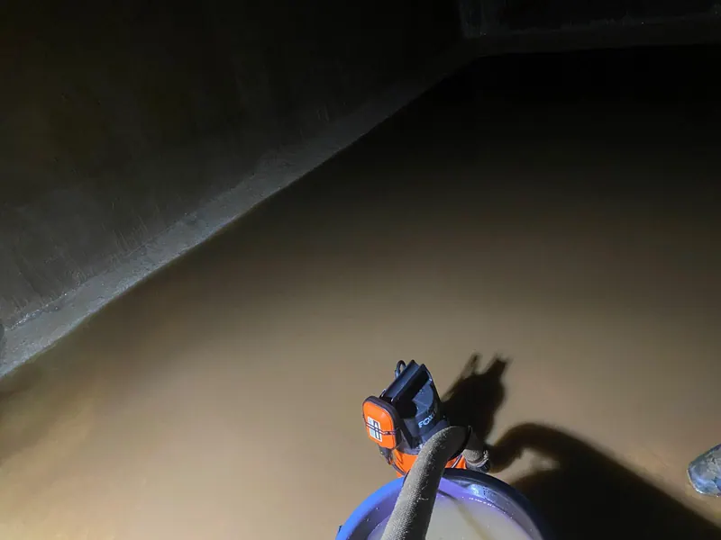 Água barrenta no fundo da cisterna de concreto, com a bomba para esvaziar, antes da limpeza