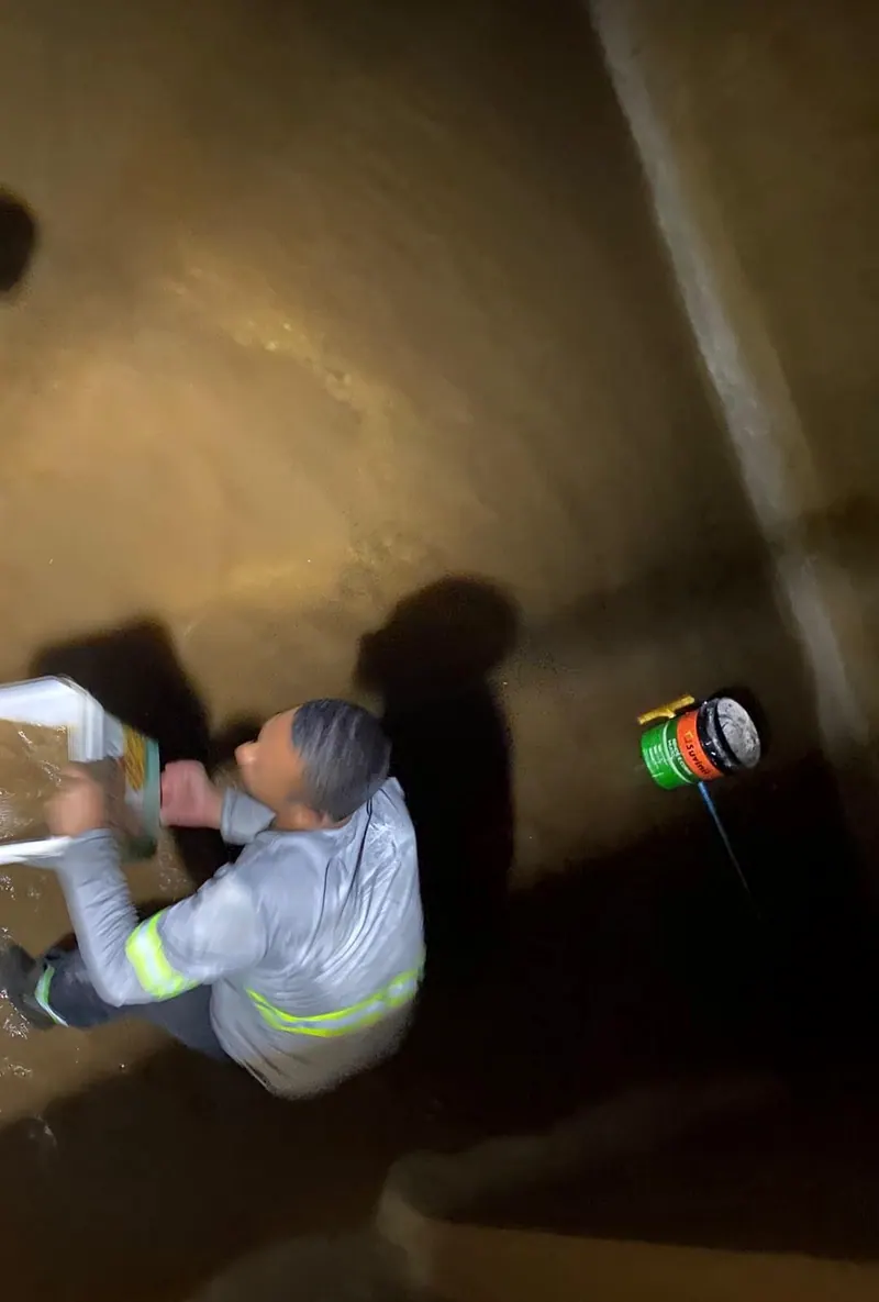 Funcionário de uniforme dentro da cisterna tirando a água barrenta com balde, visto de cima
